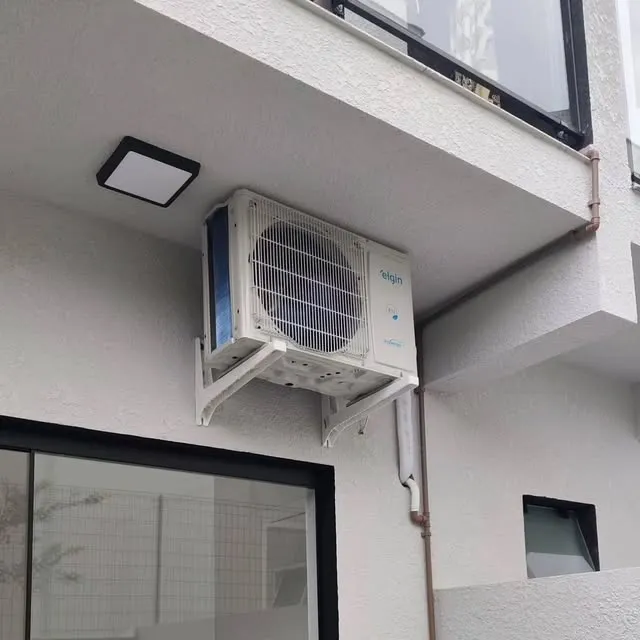 Condensadora de ar-condicionado instalada na parede externa de uma casa, abaixo da janela